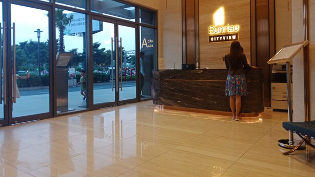Zona de recepción de un hotel con piso de mármol, mostrador de recepción y un cartel que dice "Sunrise Cityview".