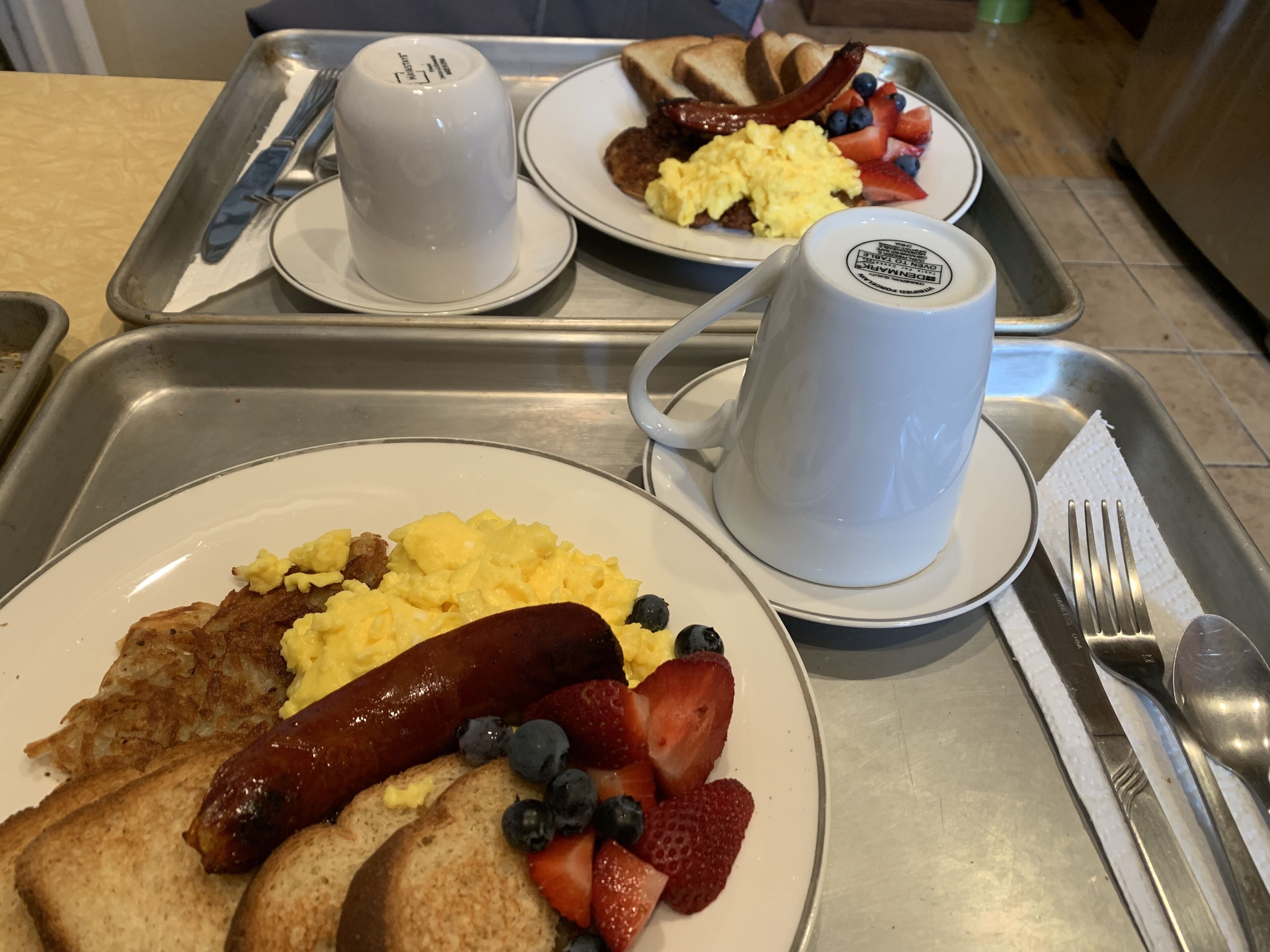 A breakfast tray with scrambled eggs, sausages, strawberries, blueberries, toast, and a mug.