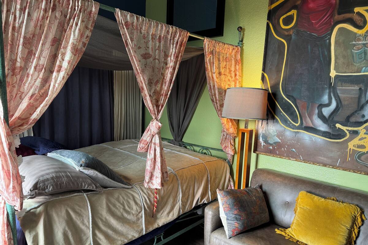 A bed with a canopy, a sofa with a cushion, and a painting on the wall.