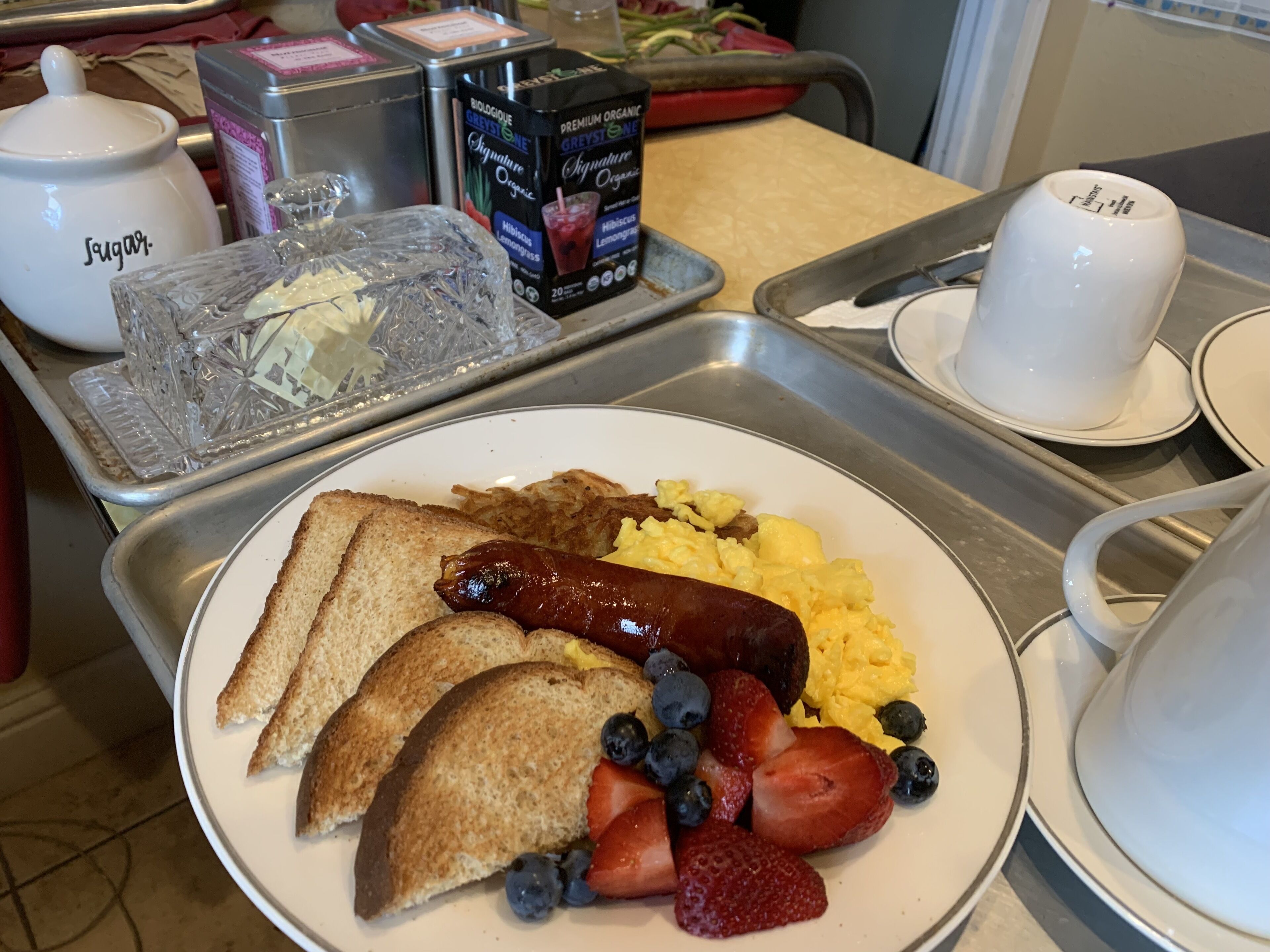 A breakfast tray with toast, scrambled eggs, sausage, strawberries, and blueberries.