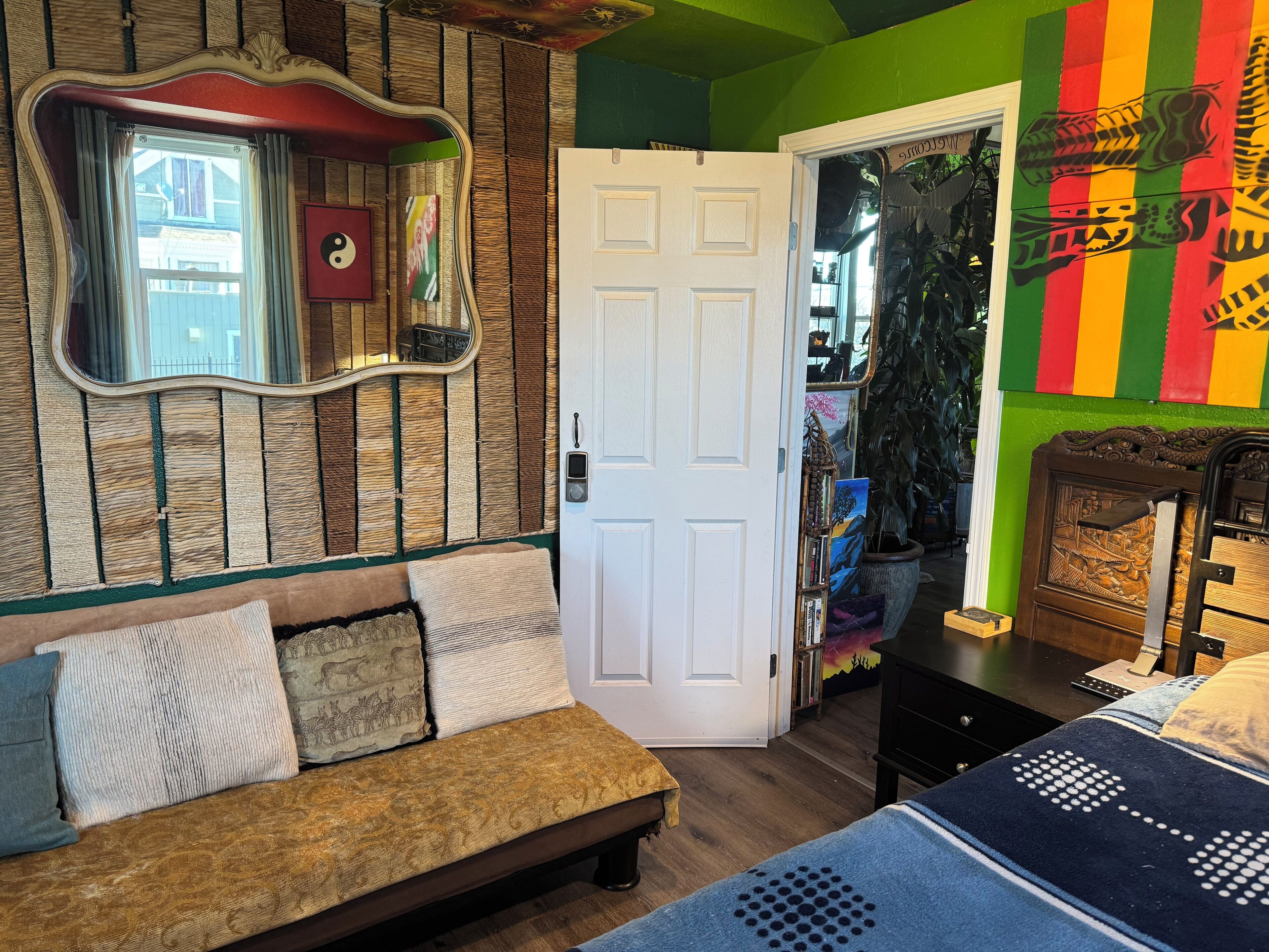 A room with a wooden wall, a white door, a sofa with patterned cushions, and a bed with a blue blanket.