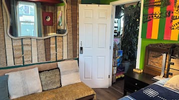 A room with a wooden wall, a white door, a sofa with patterned cushions, and a bed with a blue blanket.