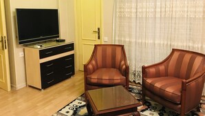 Ett vardagsrum med en platt-TV, ett träskåp, två randiga fåtöljer och en mönstrad matta.