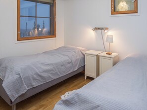 Une chambre avec deux lits simples, une table de chevet, une lampe et une fenêtre donnant sur les arbres.