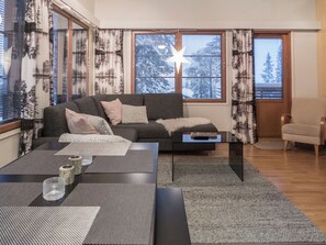 Un salon moderne avec un canapé, une table basse et une vue sur des arbres enneigés à travers de grandes fenêtres.