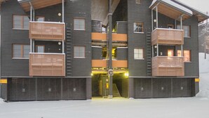 Un edificio moderno de varios pisos con balcones, una entrada cubierta y el suelo cubierto de nieve.