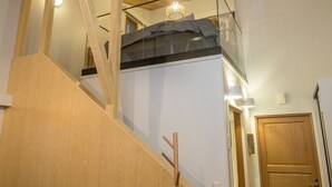 Una escalera de madera conduce a un dormitorio tipo altillo con una cama y una lámpara colgante.