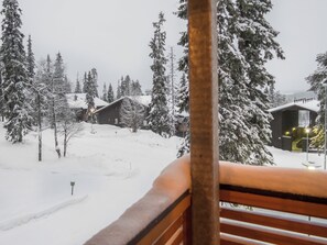 Un paysage enneigé avec un banc en bois au premier plan, une cabane et des arbres recouverts de neige.