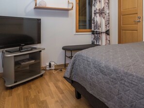 Ein Schlafzimmer mit einem Bett, einem Fernseher, einer Bank und einem Fenster mit Vorhängen.