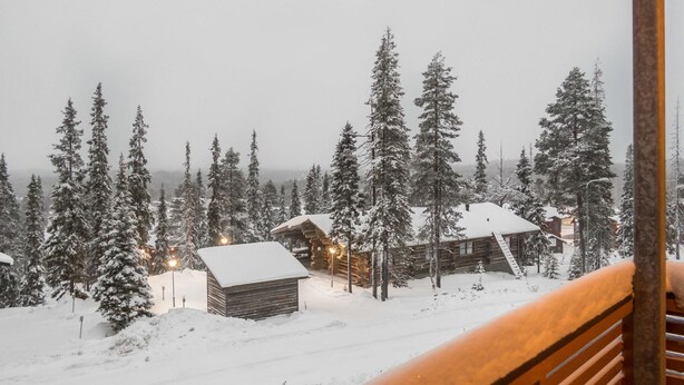 Bosque nevado con cabañas de madera y barandilla de madera.
