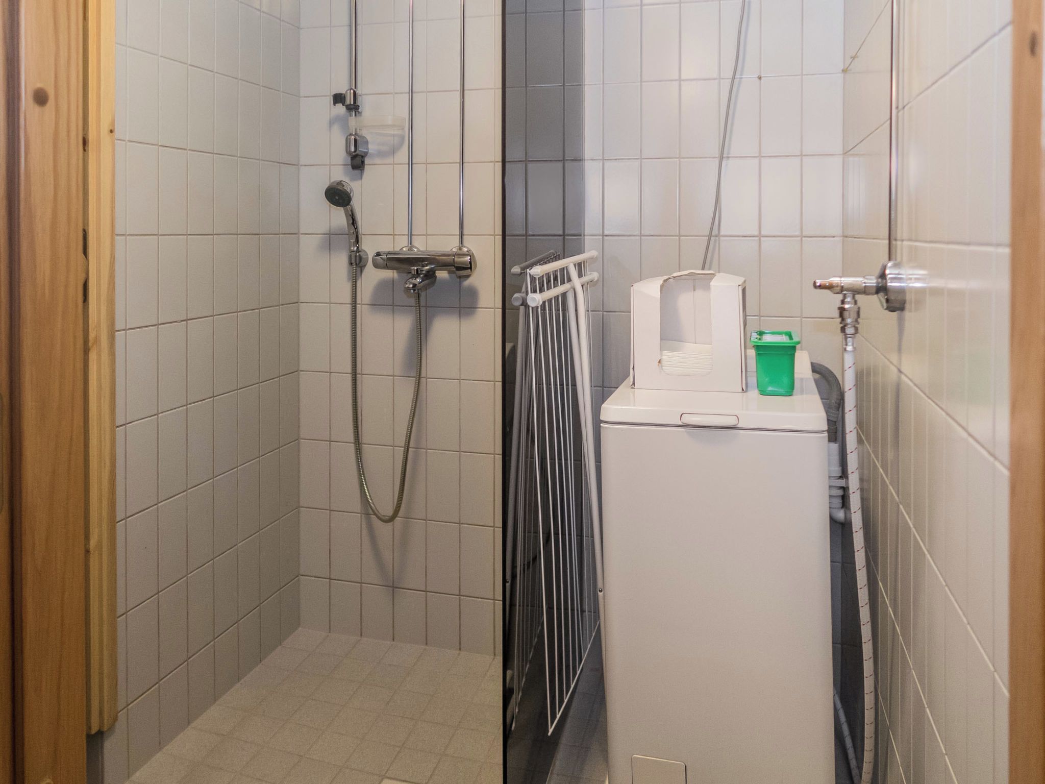 A small, tiled bathroom with a shower, a radiator, and a green bucket.