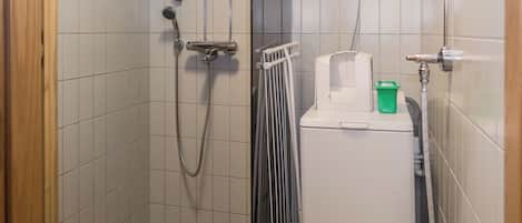 A small, tiled bathroom with a shower, a radiator, and a green bucket.