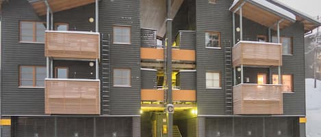 A multi-story building with a central entrance, balconies, and a snow-covered ground.