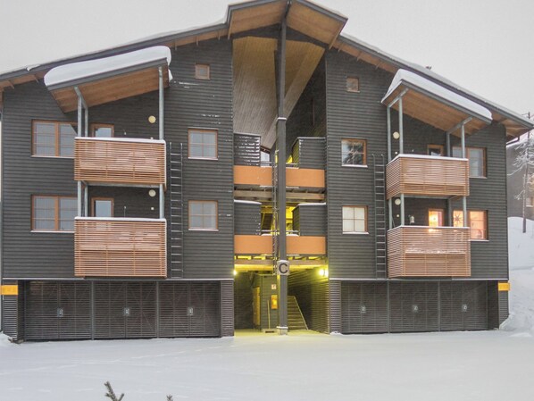 A multi-story building with a central entrance, balconies, and a snow-covered ground.