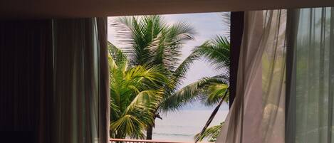 A balcony with a view of the ocean and palm trees, a hammock, and a table with a bottle and glasses.