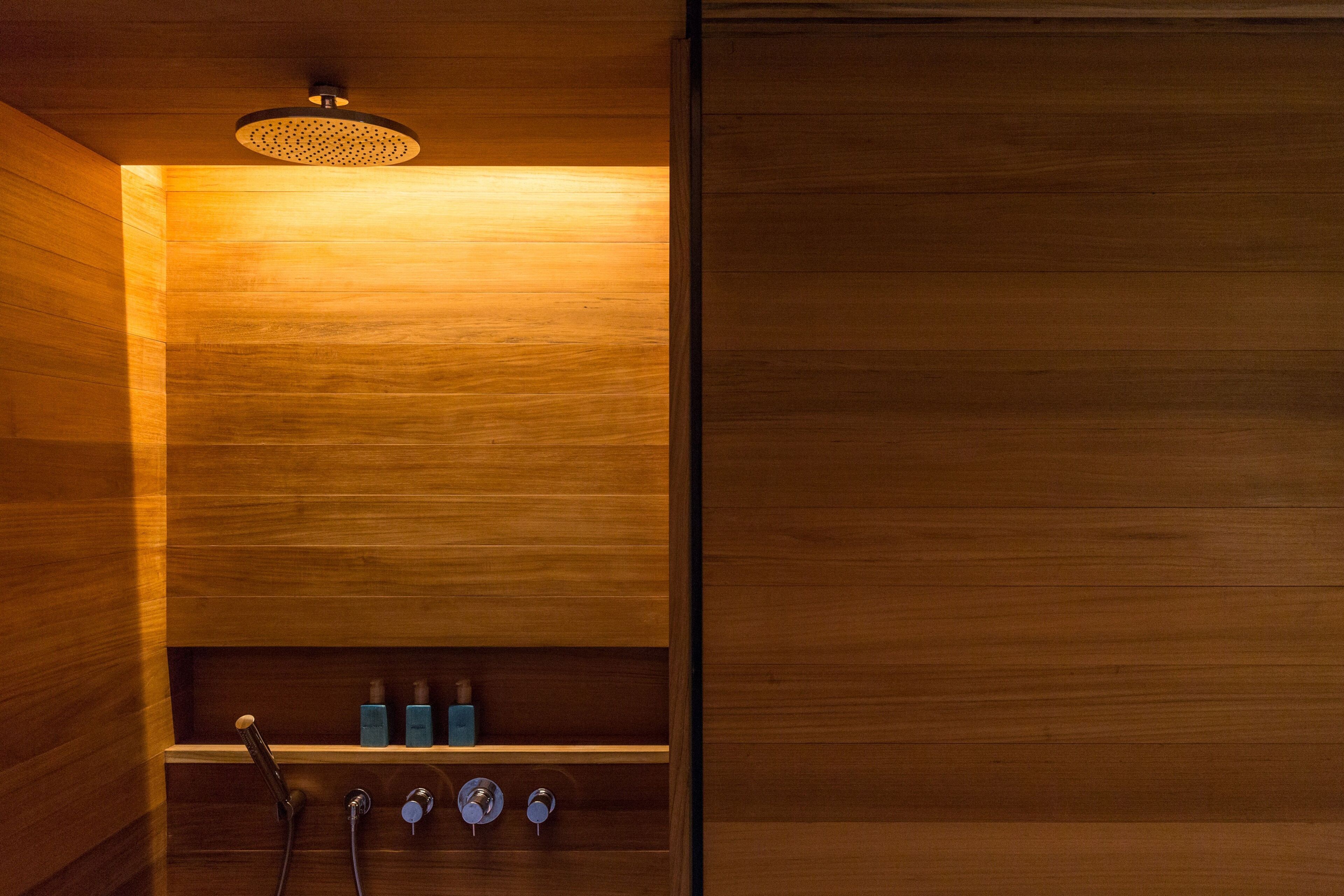 A wooden interior with a built-in shower, a shelf with toiletries, and a ceiling light fixture.