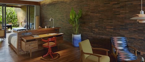 A modern room with a wooden desk, a red chair, a patterned sofa, and a large potted plant.