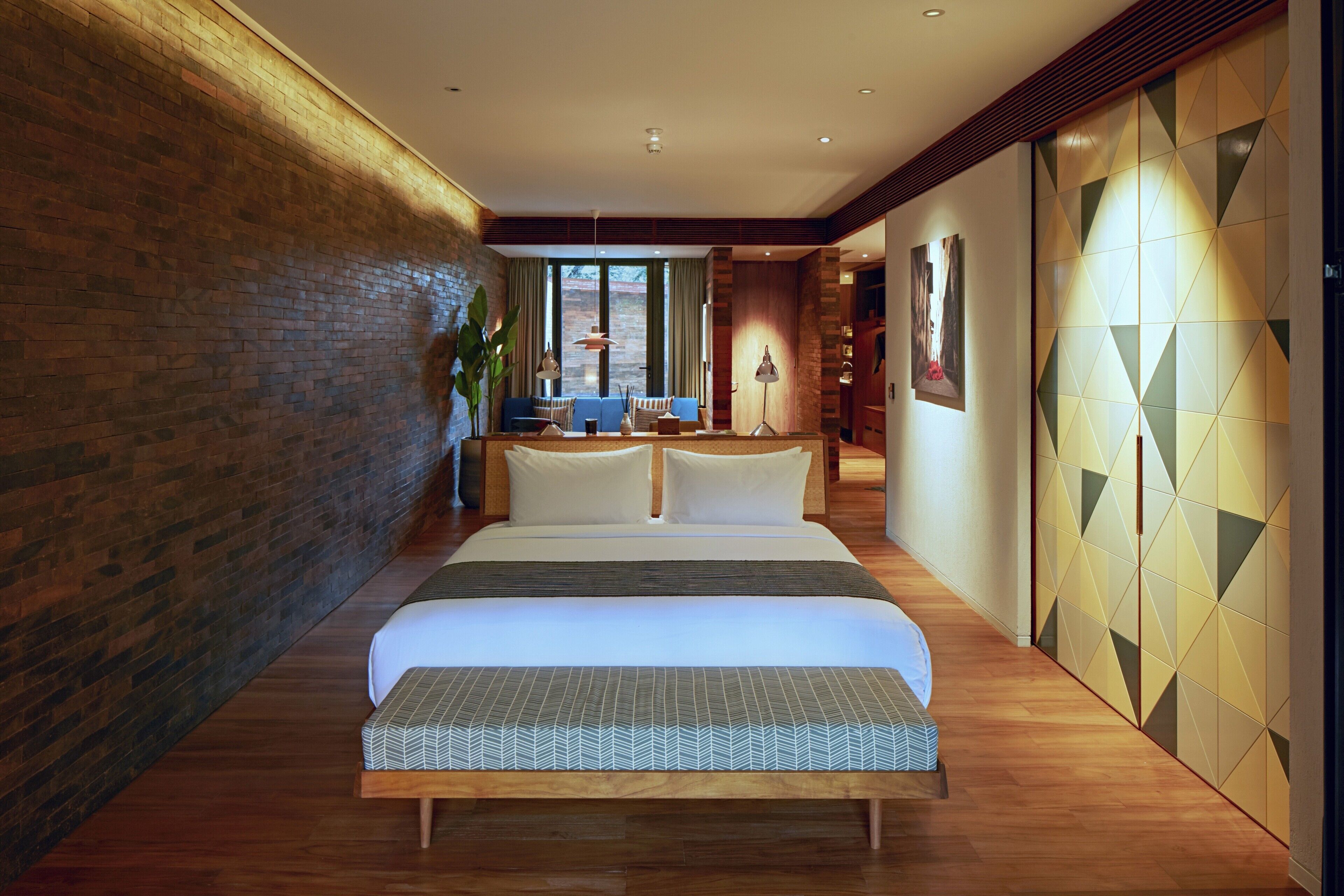 Una habitación de hotel moderna con una cama grande, suelo de madera, pared de ladrillo decorativa y un diseño geométrico en la pared.