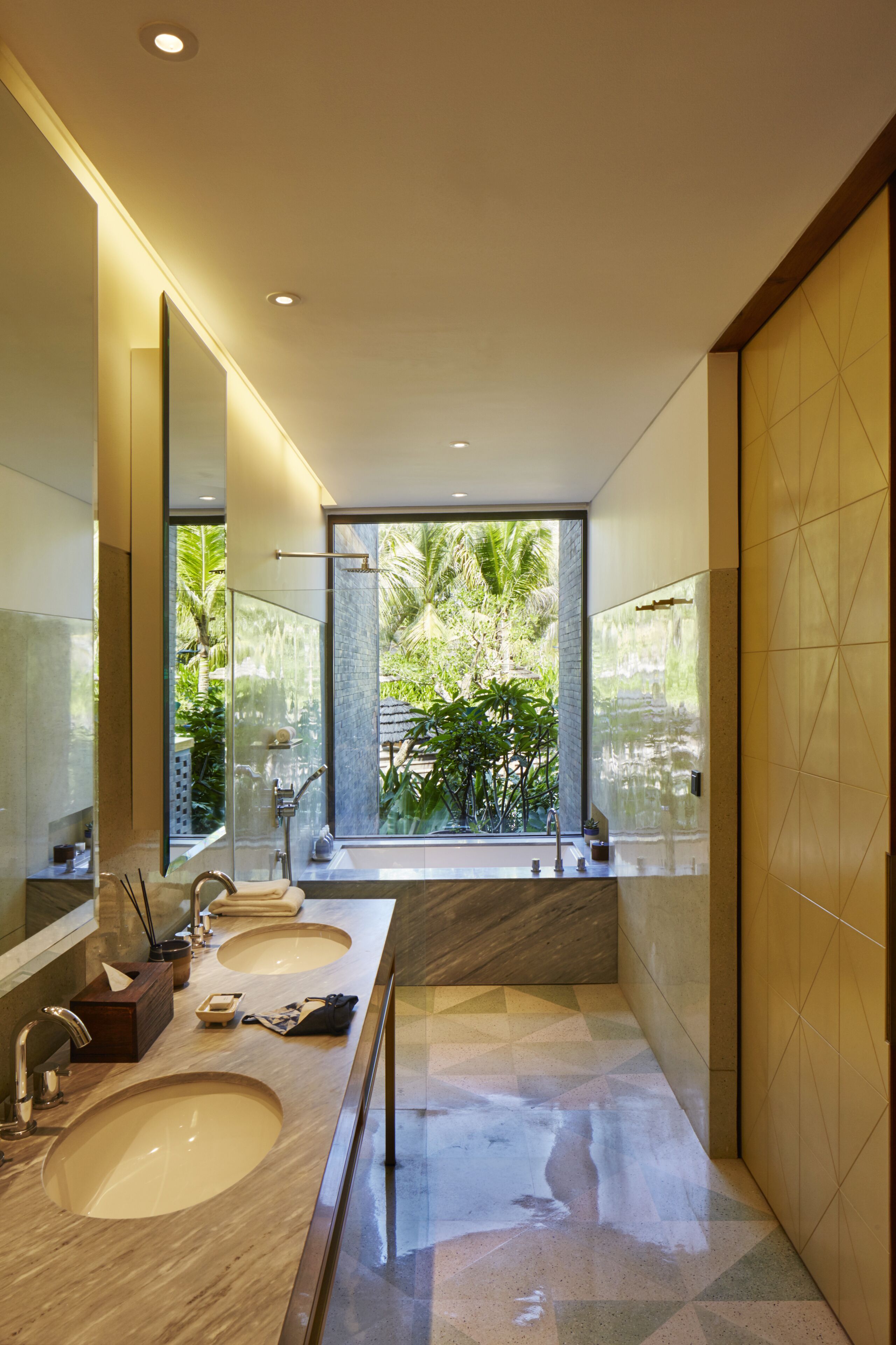Un baño moderno con dos lavamanos, un espejo grande y vistas a la vegetación exterior.