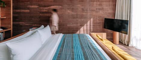 A modern hotel room with a large bed, a flat-screen TV, a wooden wall, and a bookshelf.