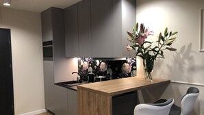Ett modernt kök med grå skåp, en köksö i trä och ett svartvitt blommönstrat stänkskydd. Det finns två vita stolar med svarta dynor.