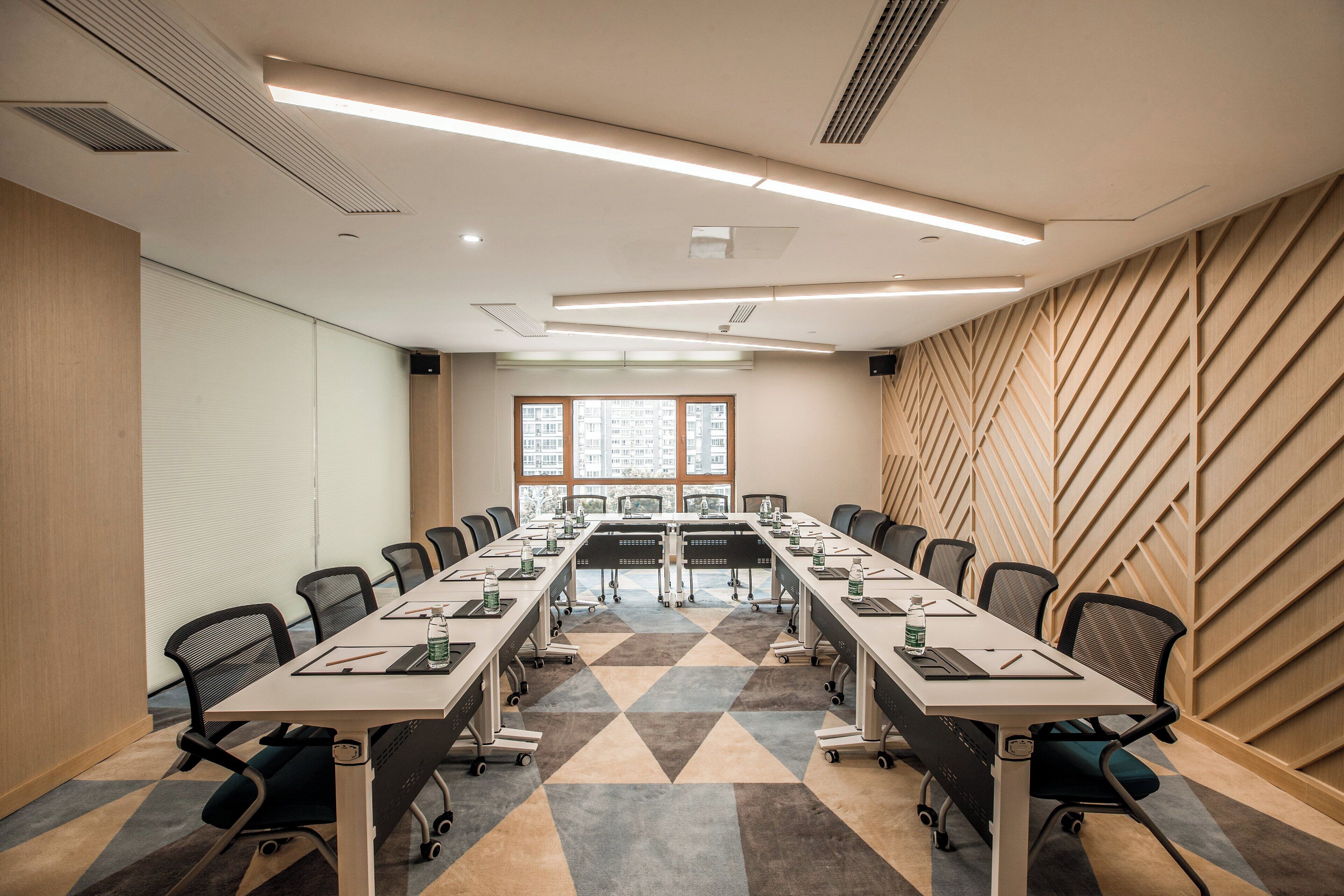 A conference room with a long table, chairs, and a view of buildings through large windows.