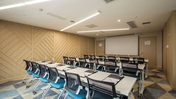A conference room with a large table, chairs, a projector screen, and a patterned wall.