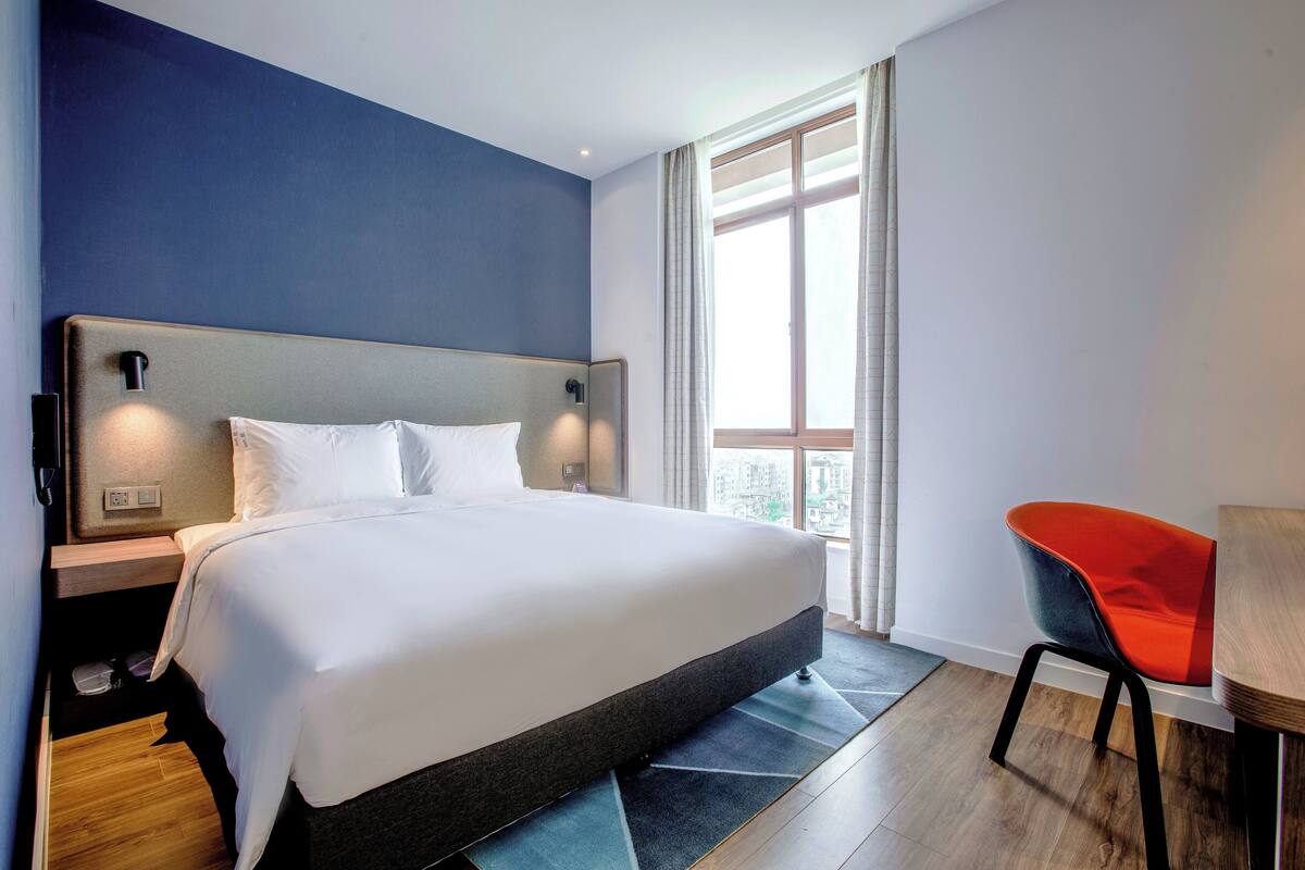 A hotel room with a large bed, a nightstand, a chair, and a window with curtains.