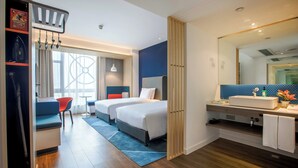 Une chambre d’hôtel avec deux lits, un bureau, une chaise, un grand miroir et une salle de bain avec un lavabo et un miroir.