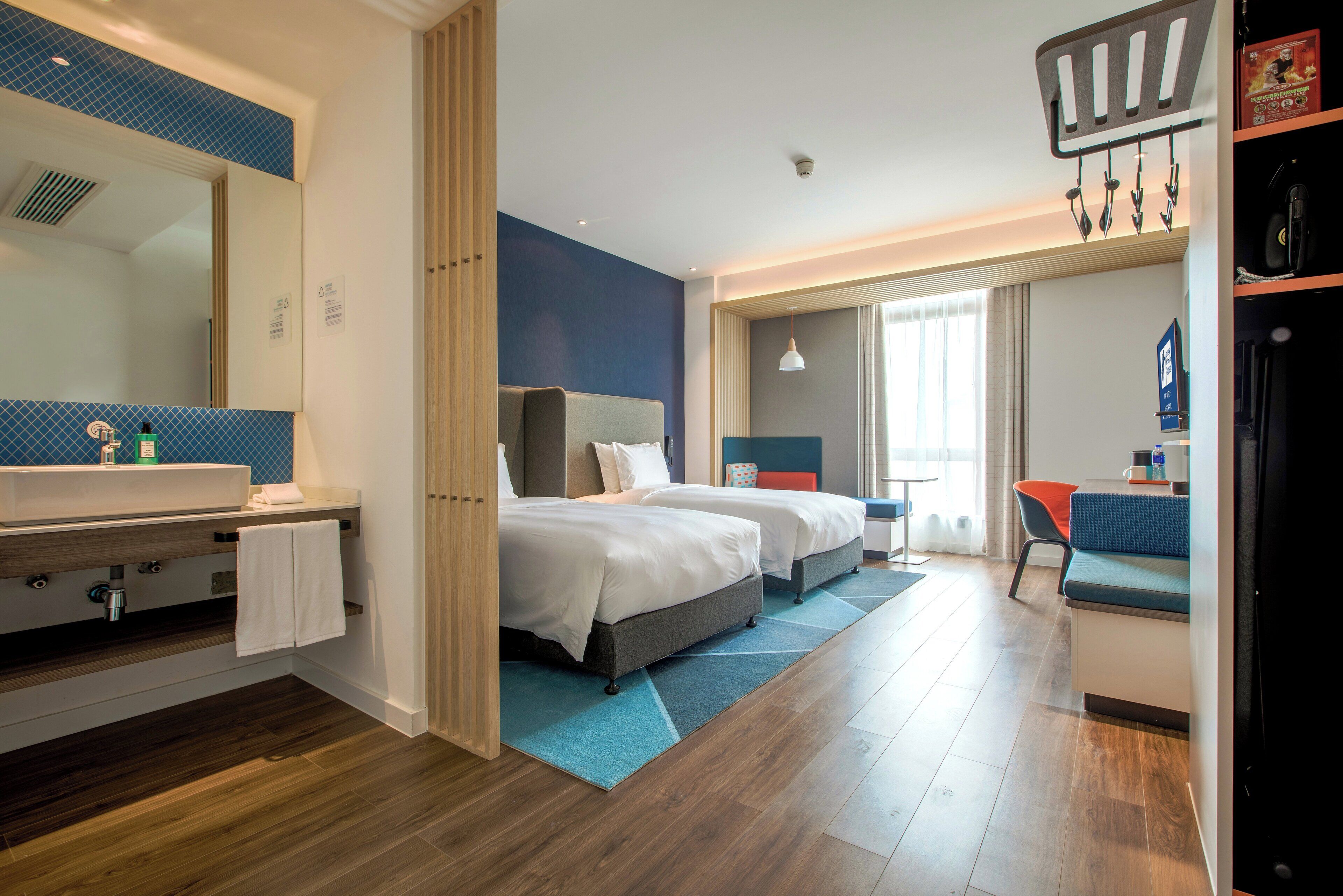 A modern hotel room with a large bathroom, two beds, a desk, and a chair.