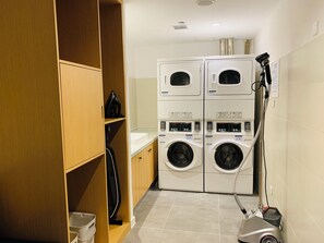 Une buanderie équipée de machines à laver et de sèche-linge superposés, d’un aspirateur et d’étagères en bois.