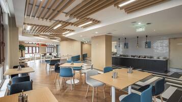 A modern restaurant with wooden ceiling beams, a kitchen area, and seating arrangements.