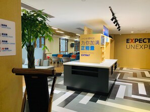 Un hall d’hôtel comprenant un comptoir d’accueil, un espace salon et un panneau indiquant la présence d’une épicerie ouverte 24 heures sur 24.