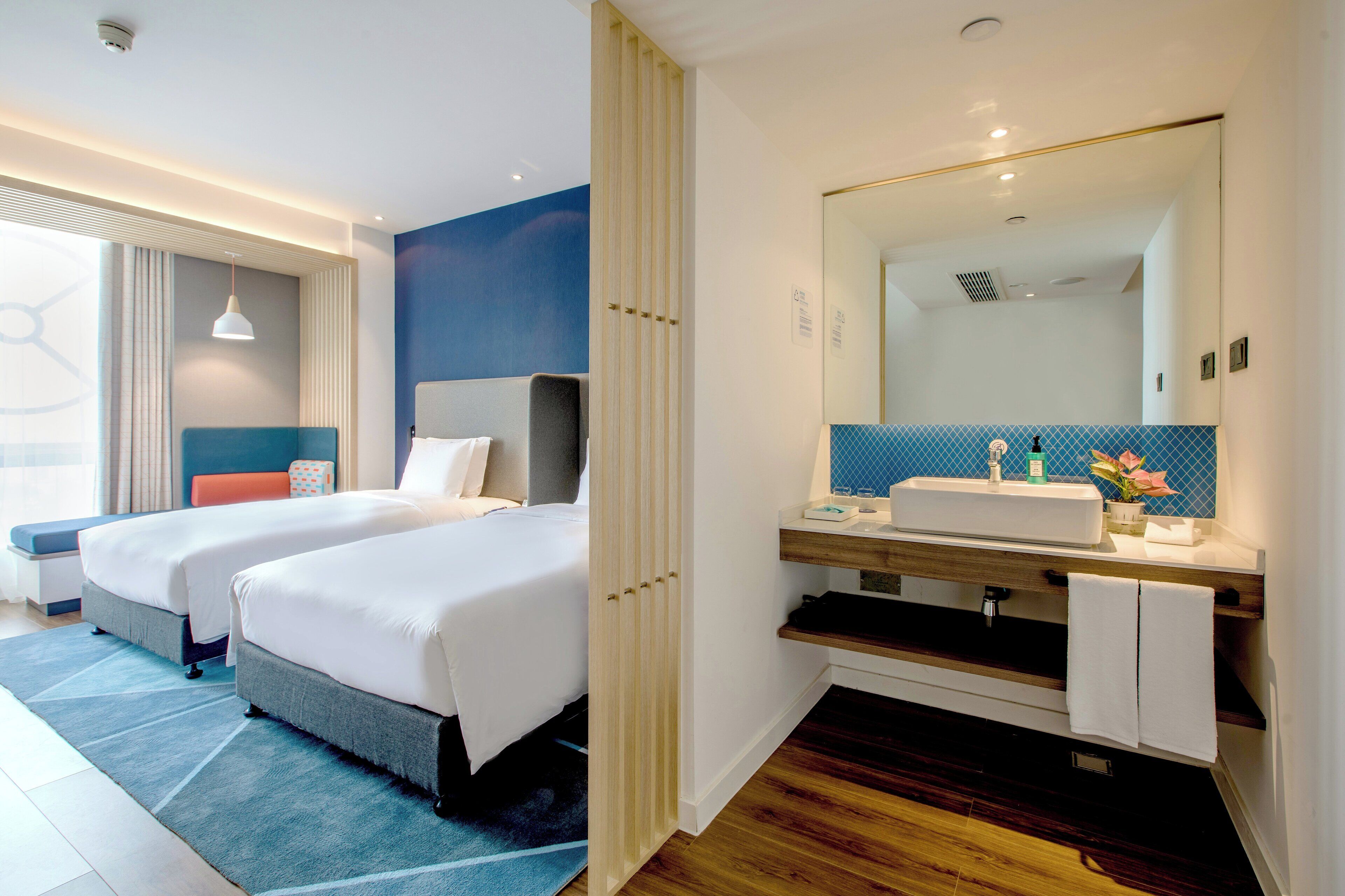 Habitación de hotel con dos camas, un espejo grande, un lavabo y una ventana con cortinas.