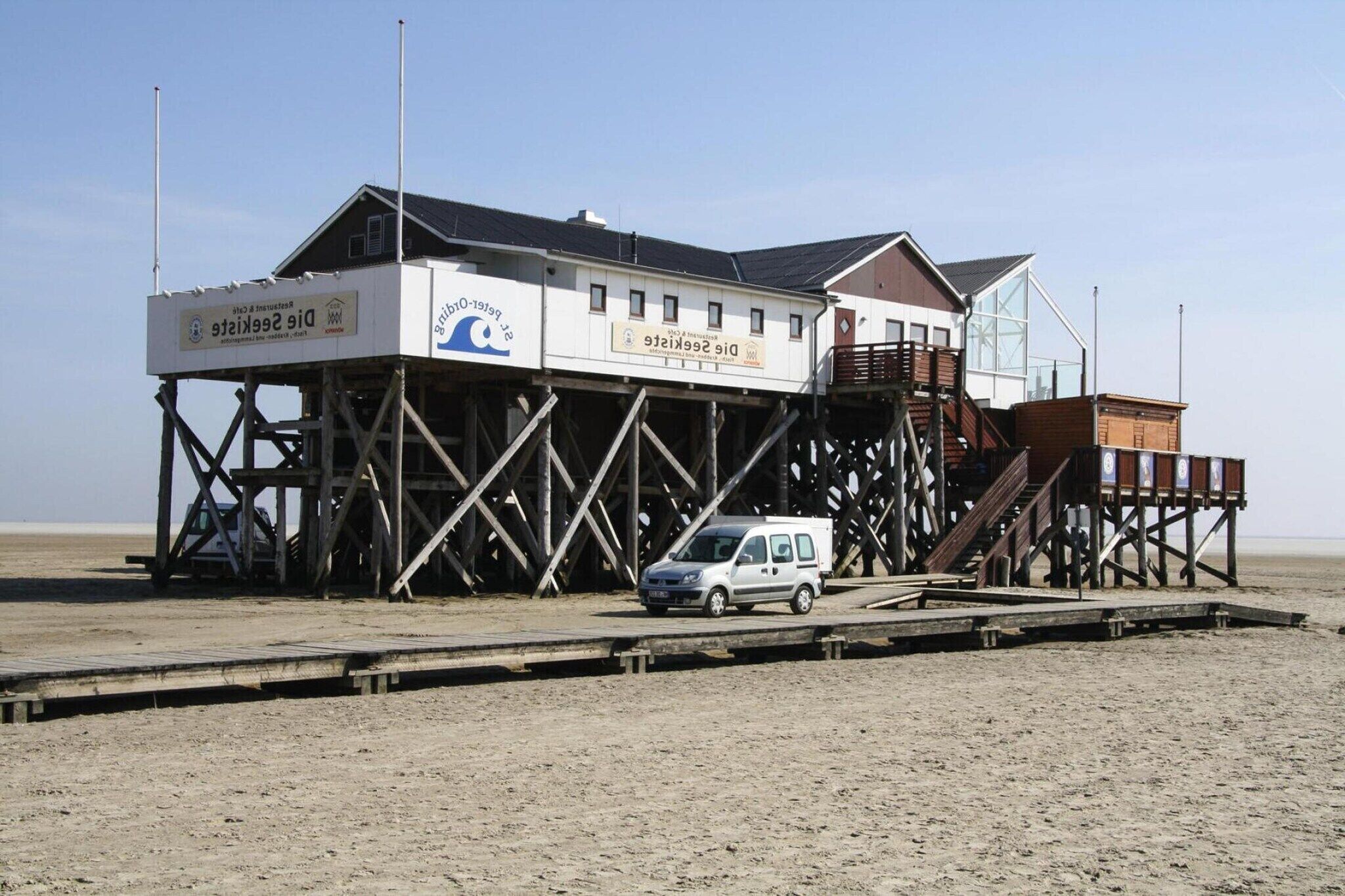 A beachside building with a wooden deck and a car parked in front.