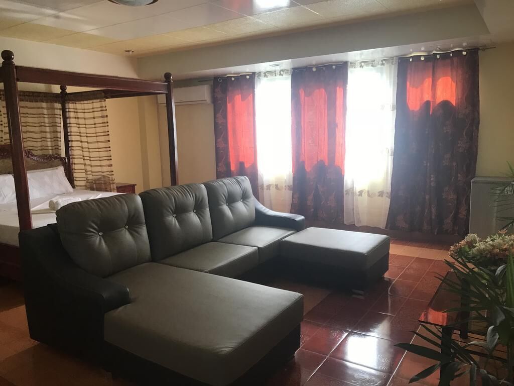 A modern living room with a sectional sofa, a four-poster bed, and a large window with red curtains.