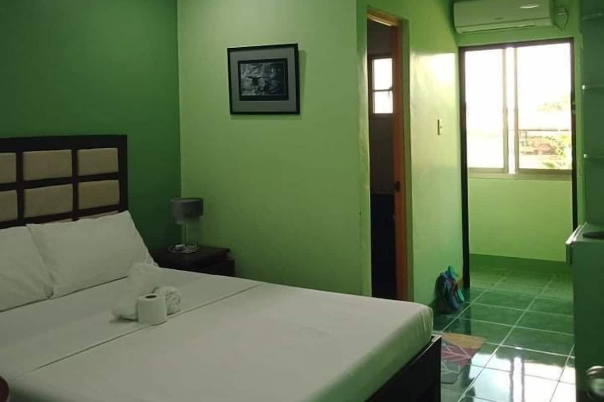 A room with a bed, a framed picture on the wall, and an air conditioning unit.