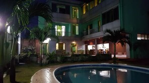 Un immeuble à plusieurs étages doté d’une piscine, de balcons et d’un éclairage extérieur.