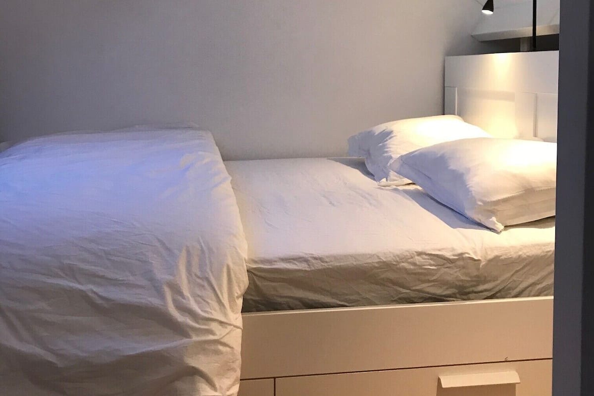A small, neatly made bed with white linens in a room with white walls and a sloped ceiling.