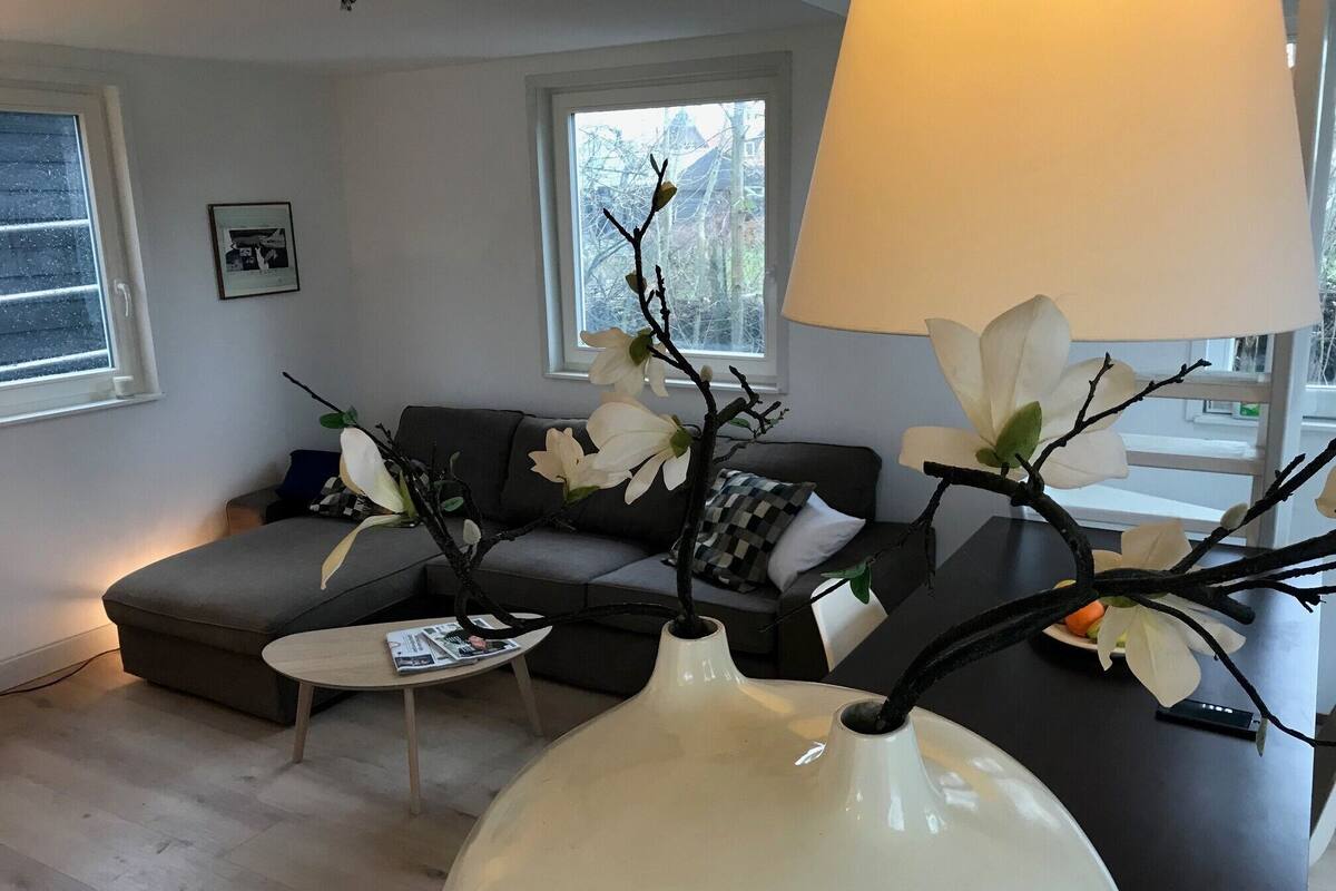 A modern living room with a grey sofa, a coffee table, and a white vase with branches and white flowers.