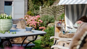 A garden patio with a table, chairs, and a striped awning.