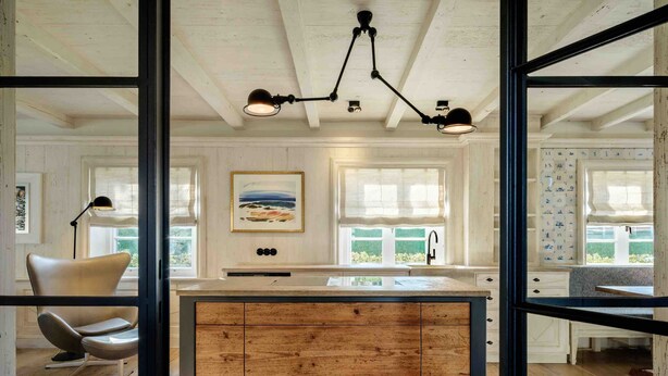 A kitchen with wooden cabinets, a central island, pendant lighting, and a view of the outdoors through windows.
