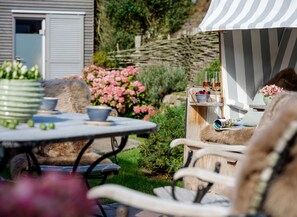 A garden patio with a table, chairs, and a striped awning. - LighthouseSoul Senhoog Luxury Holiday Homes ***** - LighthouseSoul SENHOOG (Sylt)