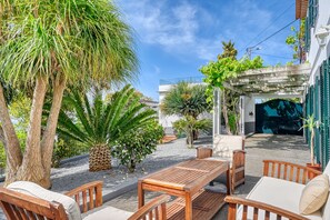 Un patio con muebles de madera, una palmera y un edificio con entrada cubierta.