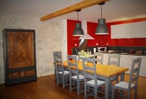 A dining area with a wooden table and six chairs, a large cabinet, and a red and white kitchen in the background.
