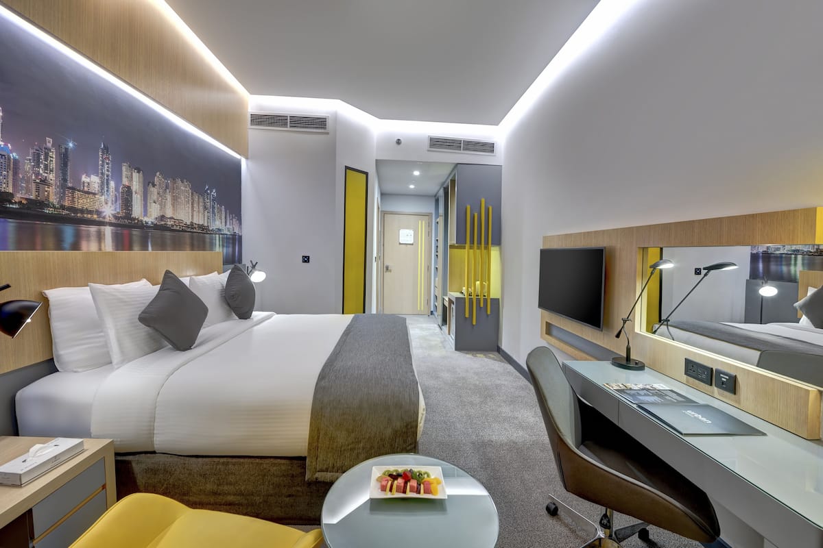 Ein modernes Hotelzimmer mit einem großen Bett, einem Schreibtisch, einem Stuhl und einem Esstisch mit einer Schüssel Essen.