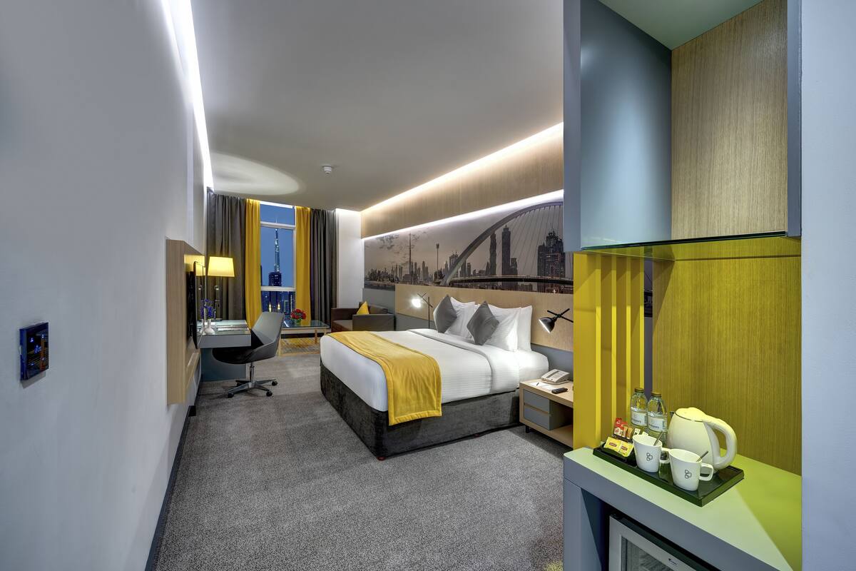 Ein modernes Hotelzimmer mit Bett, Nachttisch, Schreibtisch, Stuhl und einer Stadtansicht als Wandgemälde.