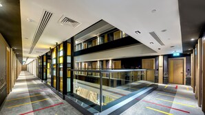 Een moderne hotelgang met glazen balustrade, boekenkasten en een helder uitzicht op de stad door de ramen.