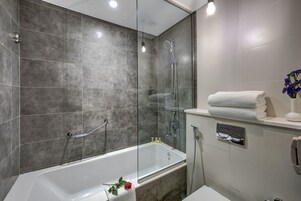 Un baño moderno con ducha envuelta en vidrio, una bañera blanca y un tocador con un perchero y un florero.