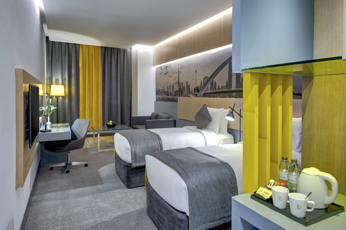 Ein Hotelzimmer mit zwei Betten, einem Schreibtisch mit Stuhl, einer Schreibtischlampe, einer Kaffeemaschine und einem Tablett mit Tassen und Wasserkocher.